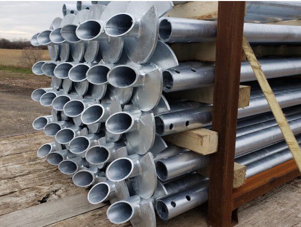 A banded stack of galvanized helical screw piles showing the helix plates and shaft bolt holes